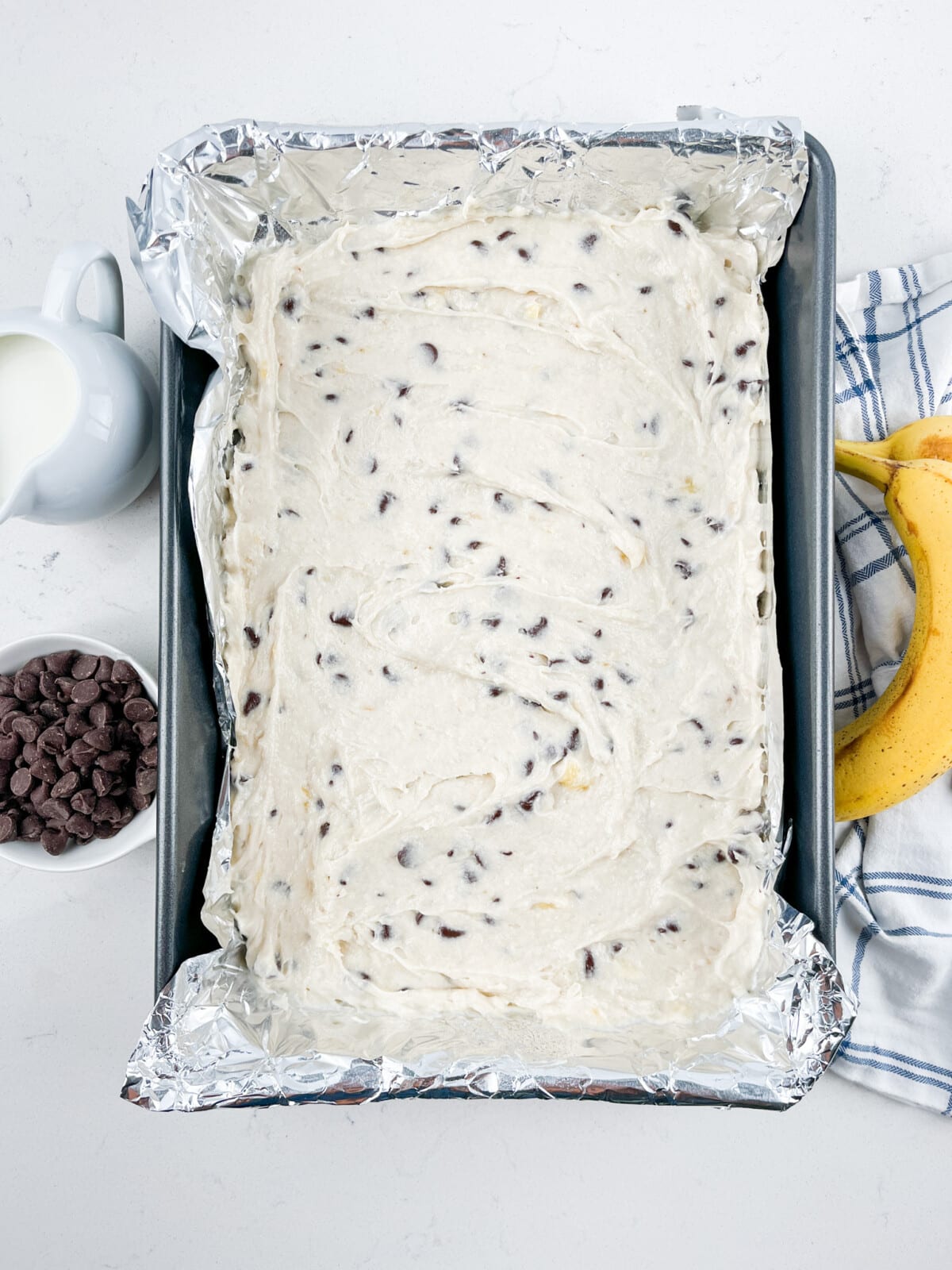 banana bar dough with chocolate chips in pan lined with foil.
