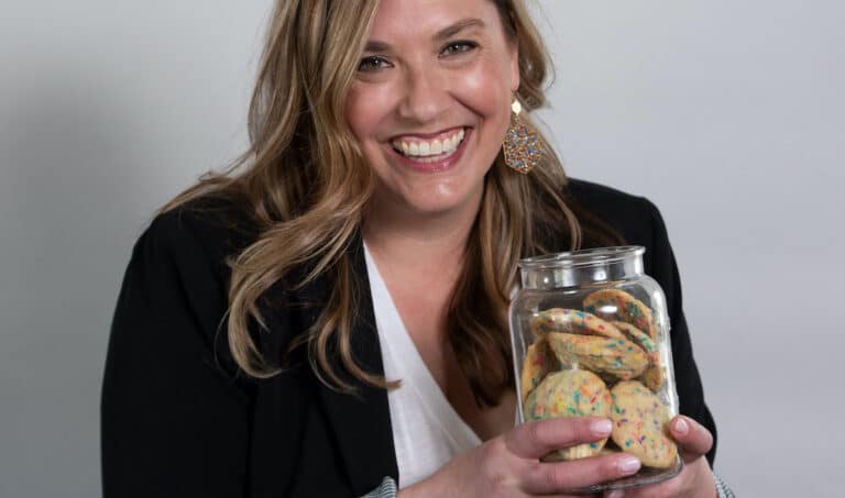 woman smiling wearing blazer and holding cookie jar full of sprinkle cookies