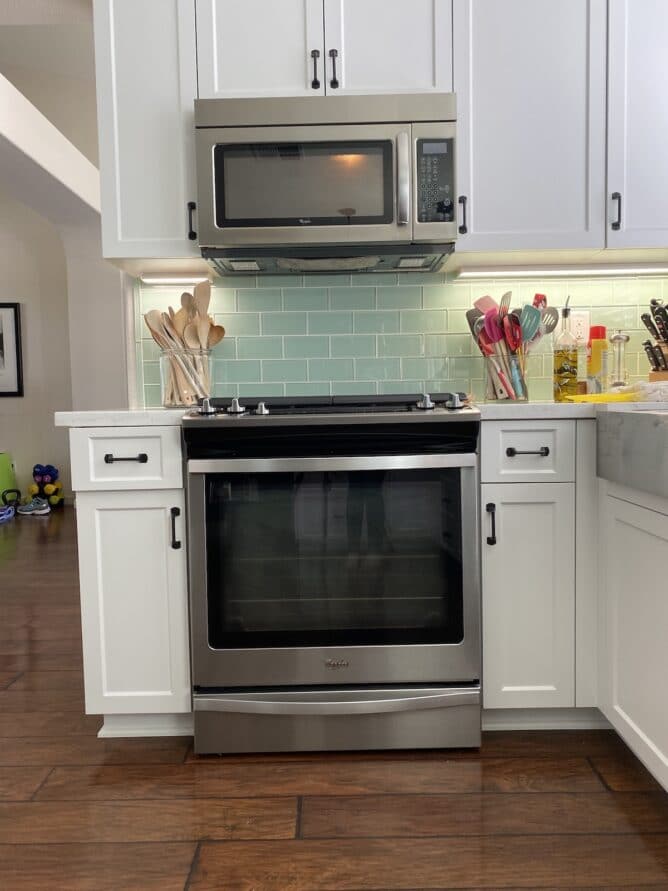 oven in kitchen with white cabinets and green backsplash