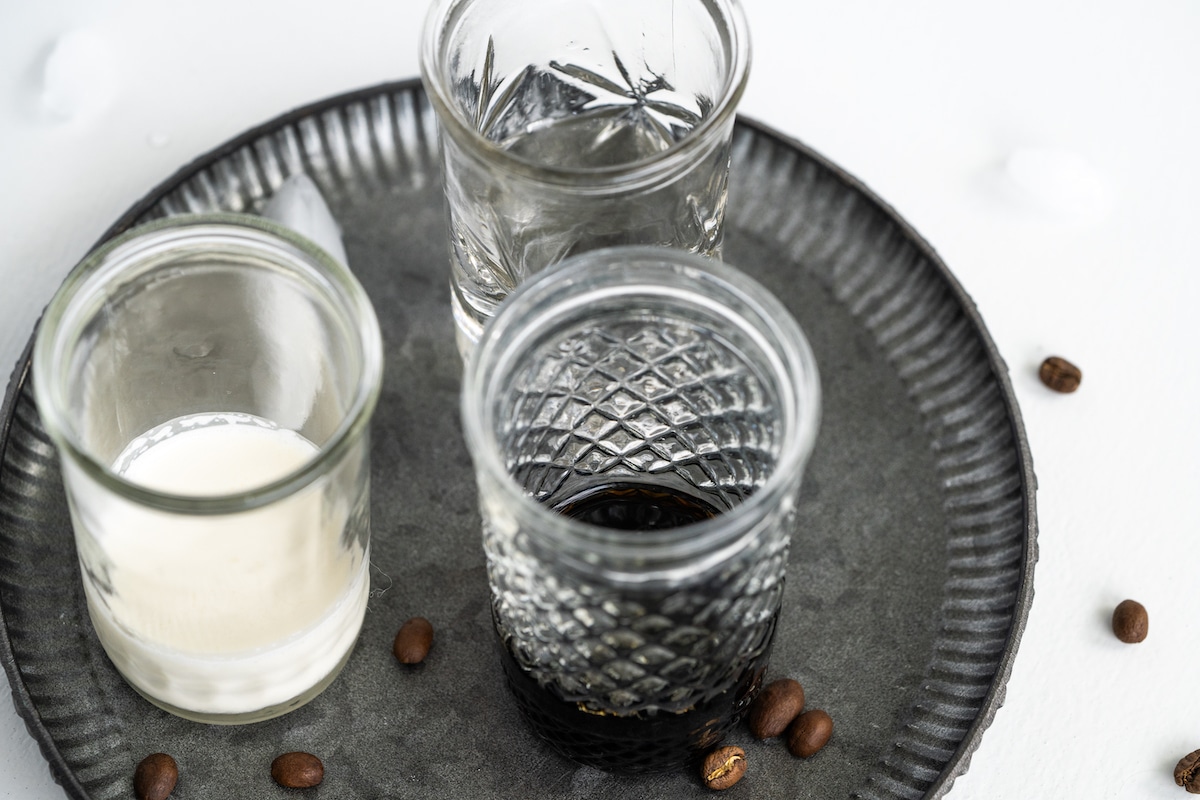 Overhead shot of the ingredients for white russian in glasses on a metal tray