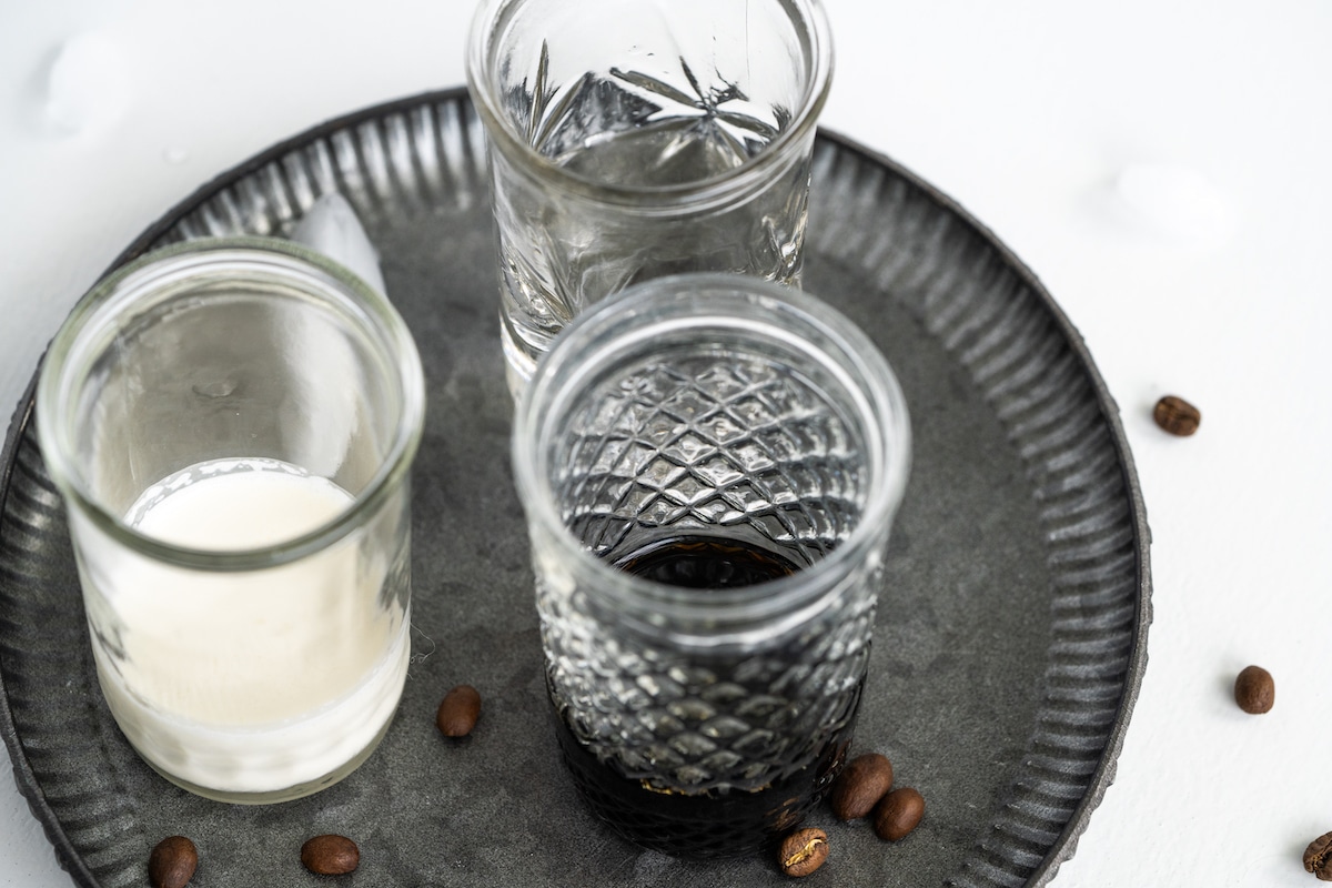 Overhead shot of the ingredients for white russian in glasses on a metal tray