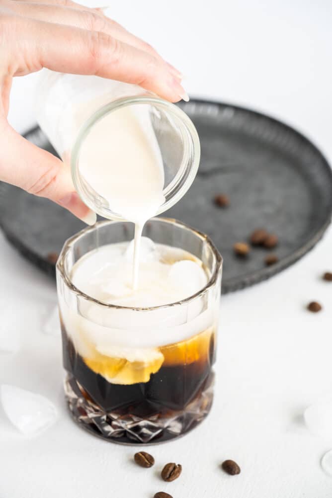Cream being poured into cocktail glass to finish making a white russian