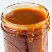 An open glass jar filled with thick caramel sauce, made from a classic caramel recipe, with caramel dripping down the sides.