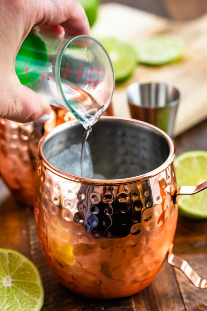 Shot of vodka being poured into a moscow mule mug