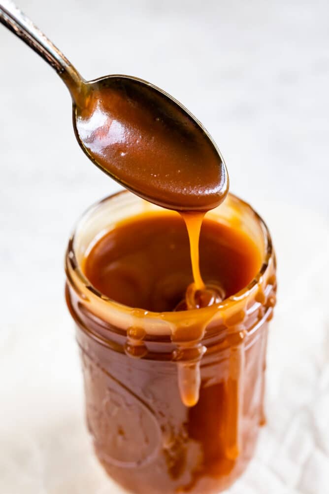 Spoonful of easy caramel sauce coming out of mason jar of sauce