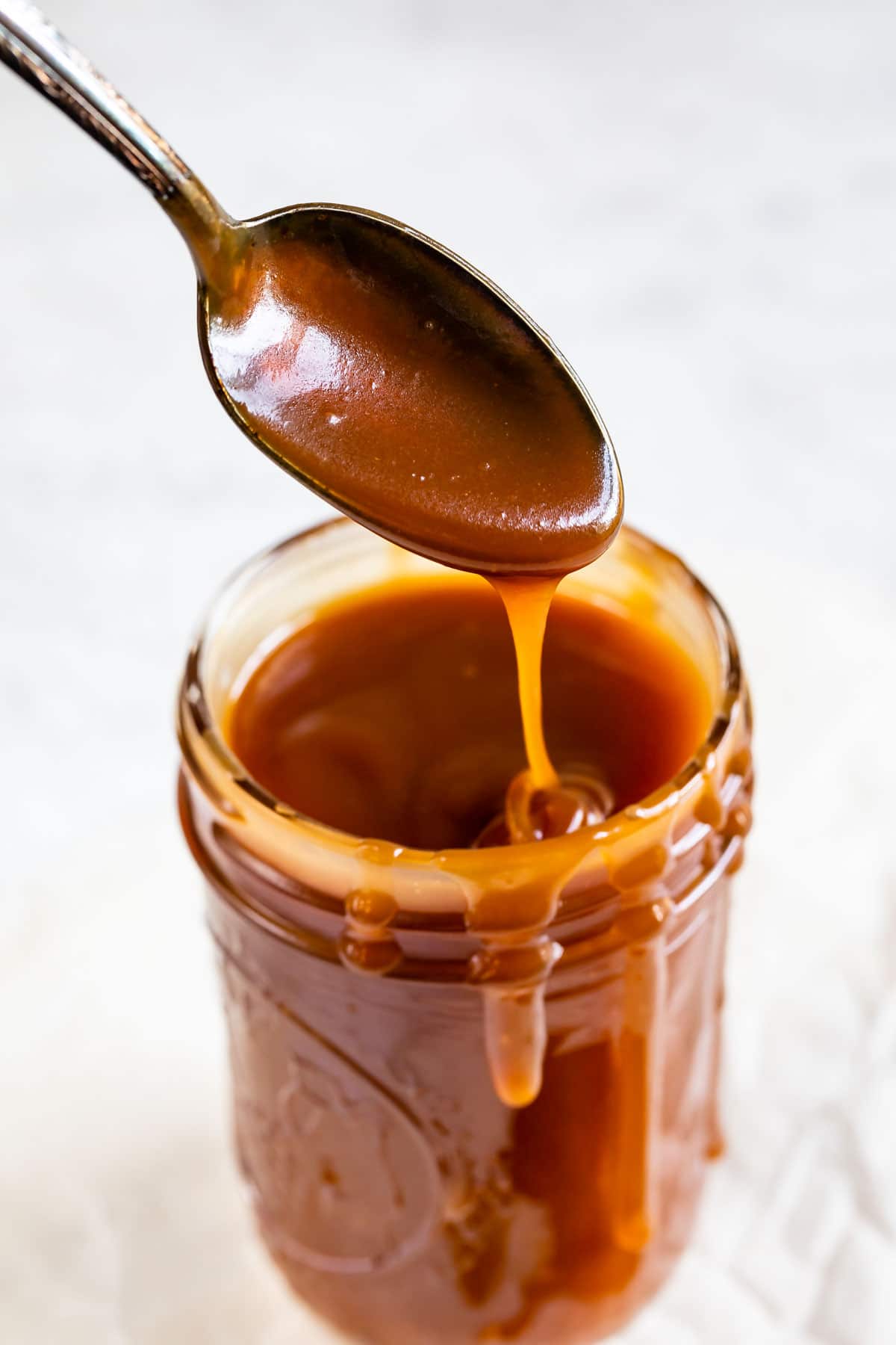 Spoonful of easy caramel sauce coming out of mason jar of sauce