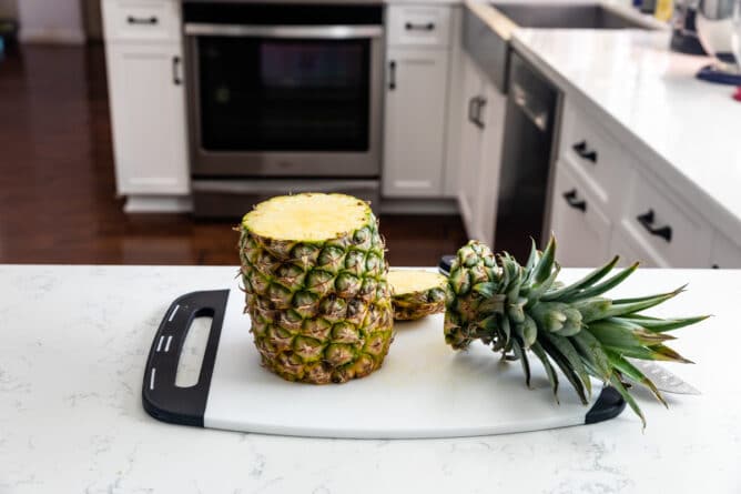 pineapple with top and bottom cut off on white cutting board