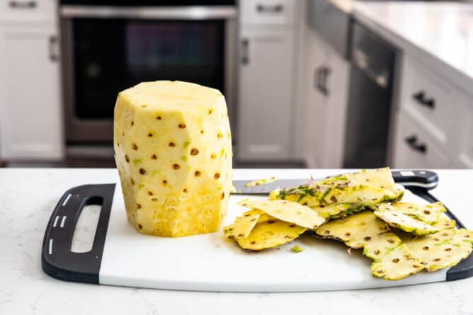 pineapple without skin on white cutting board with scraps next to it