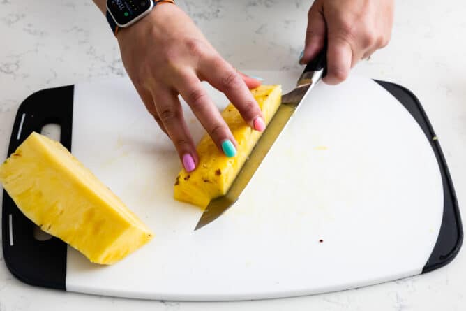 hands slicing pineapple into chunks on white cutting board