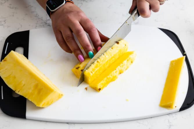 hands slicing pineapple into chunks on white cutting board