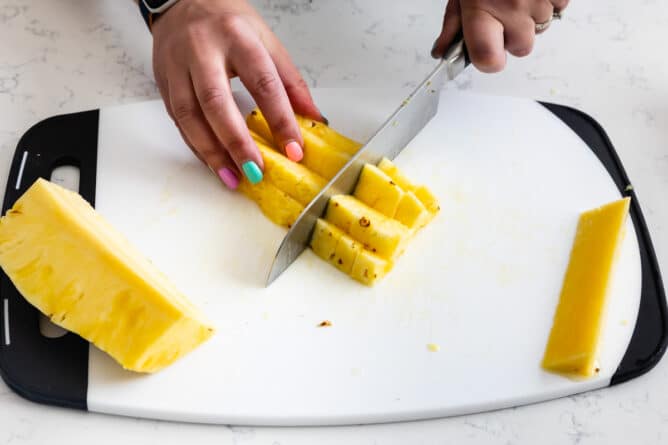 hands slicing pineapple into chunks on white cutting board