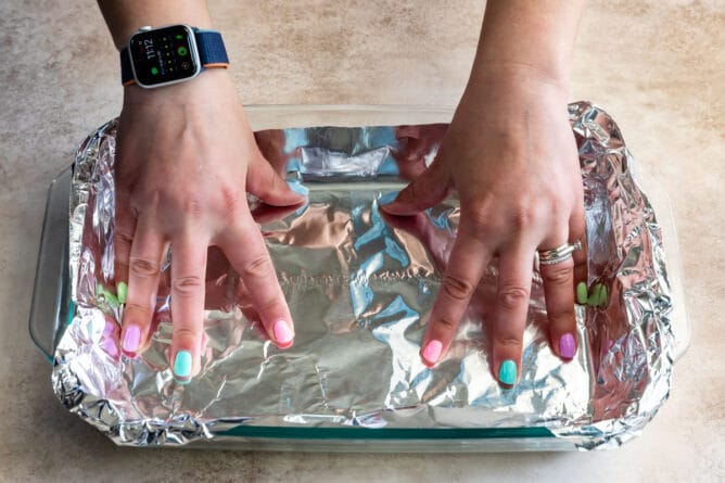 hands in 9x13 pan pressing foil into bottom of pan