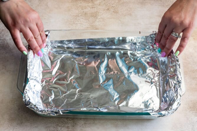 hands pressing foil into the corners of a 9x13 pan