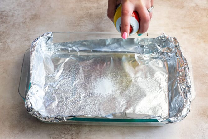 hand spraying pam on foil in 9x13 pan