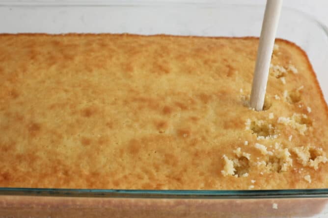 cake in pan being poked with wooden spoon