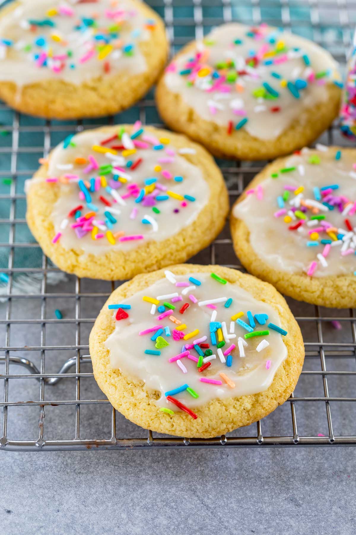 Five sugar cookies with icing and sprinkles on a wire cooling rack