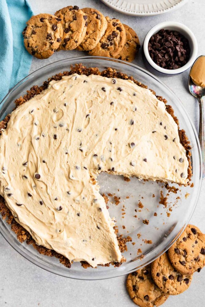 Overhead shot of chocolate chip peanut butter pie with one slice missing and chocolate chip cookies around the pie