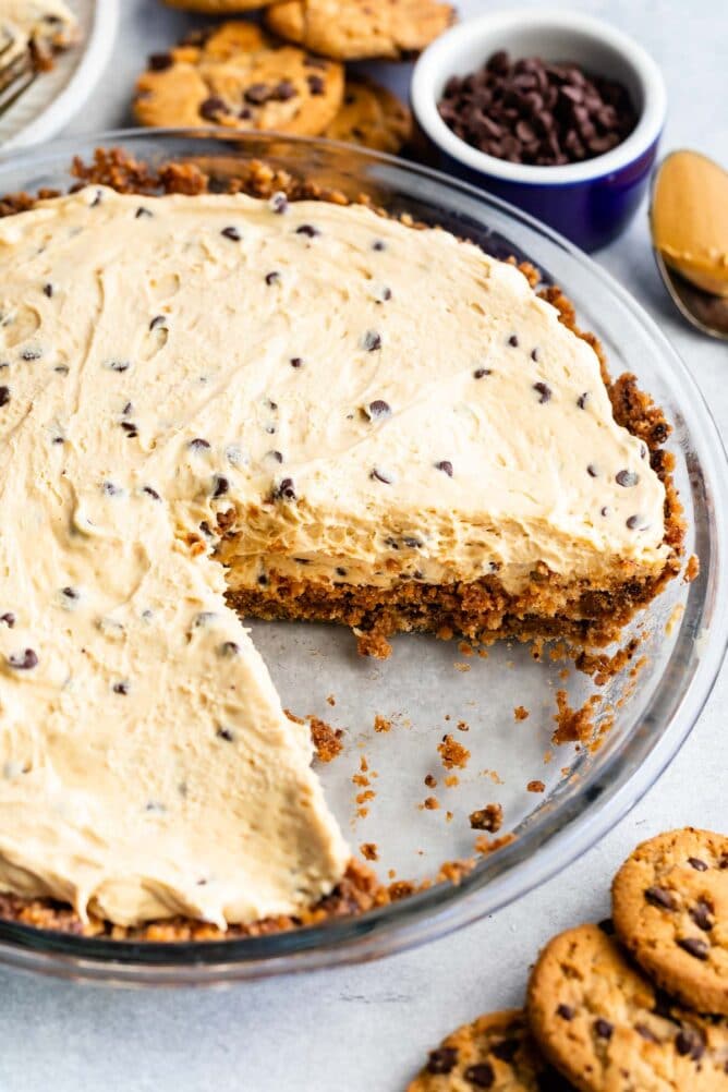 Close up overhead shot of chocolate chip peanut butter pie with one slice missing and chocolate chip cookies around the pie