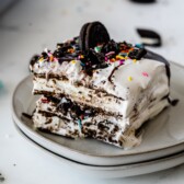 One slice of ice cream sandwich cake on a plate with sprinkles and an oreo on top