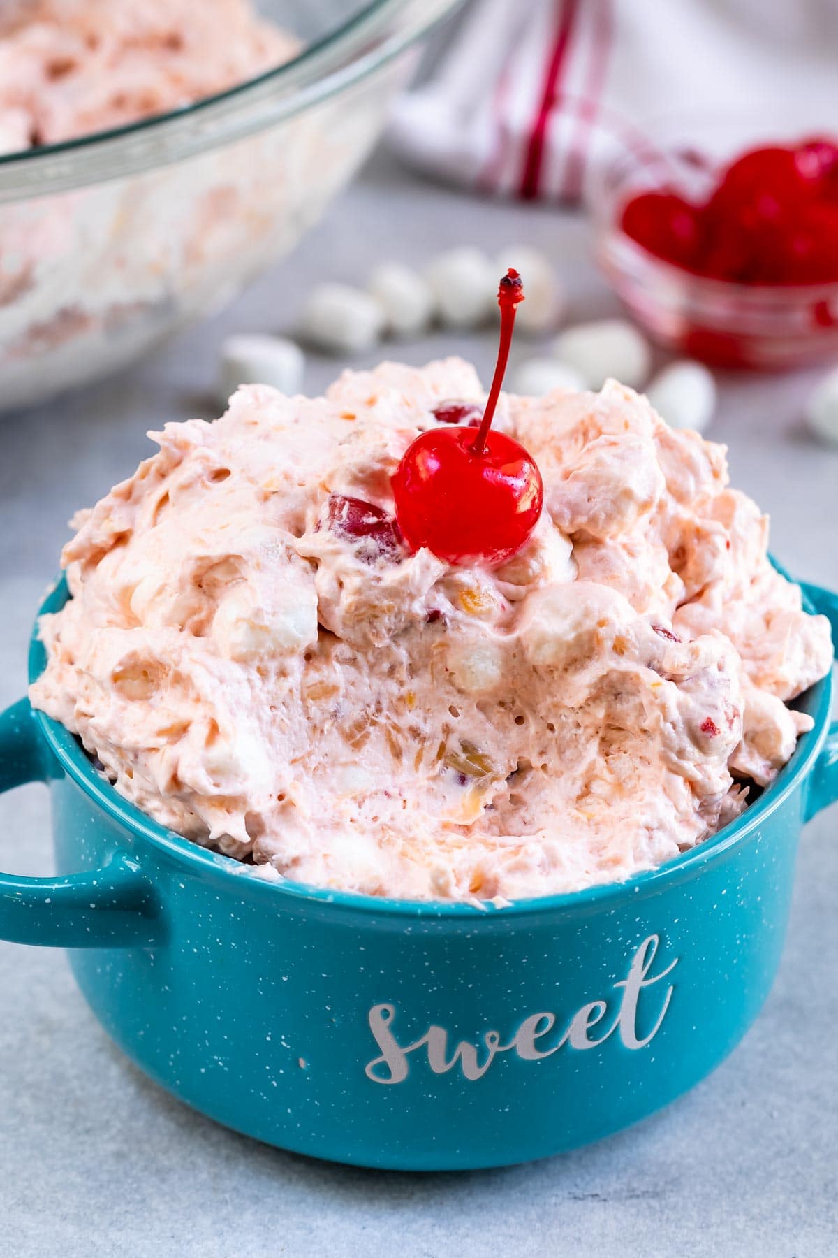 Turquoise mug filled with cherry fluff with a cherry on top and one big spoonful missing