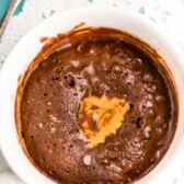 overhead shot of chocolate cookie in a white mug with peanut butter on top of a doilies and blue background