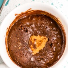 overhead shot of chocolate cookie in a white mug with peanut butter on top of a doilies and blue background