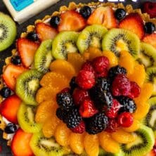 Overhead shot of no bake fruit tart with ingredients around it and recipe title on top of photo