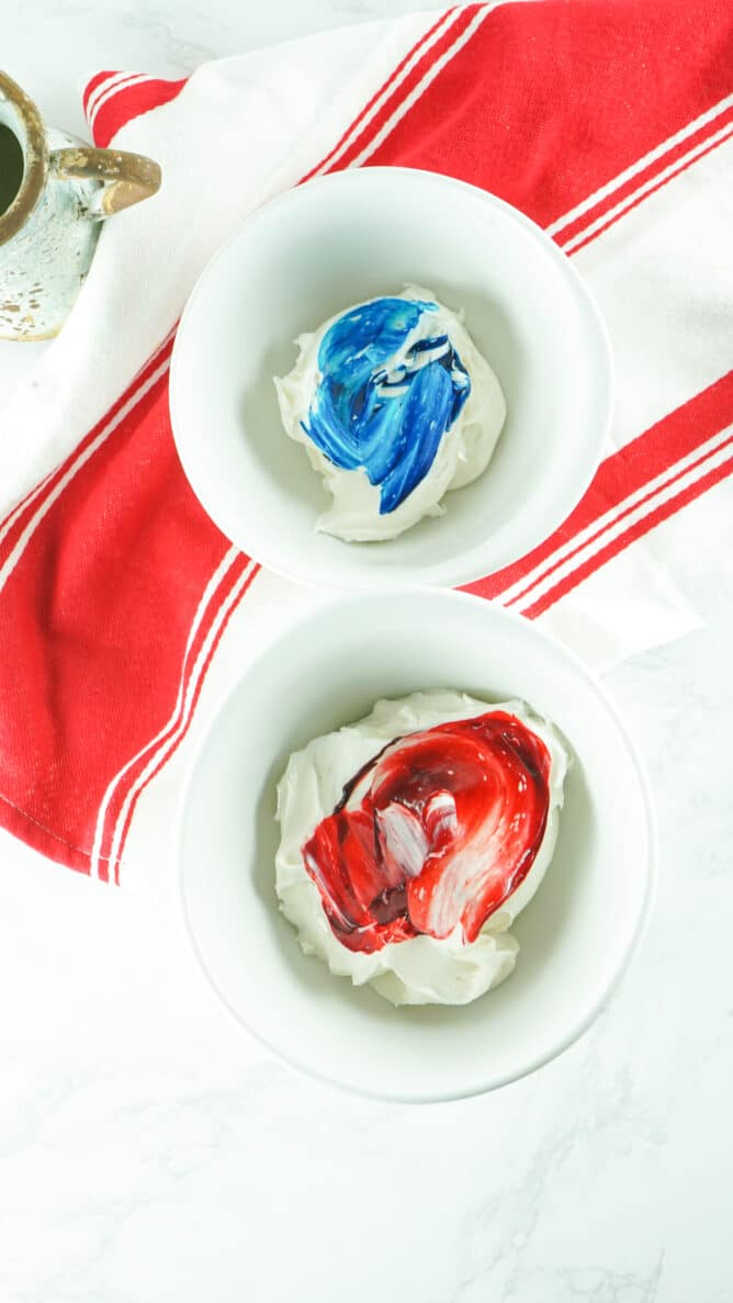 Overhead shot of two bowls of icing being mixed with blue and red food coloing