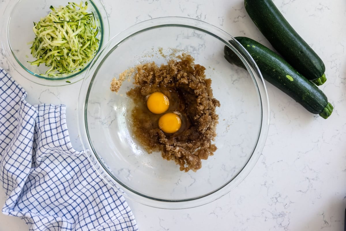 clear bowl with zucchini batter and eggs with zucchini around.