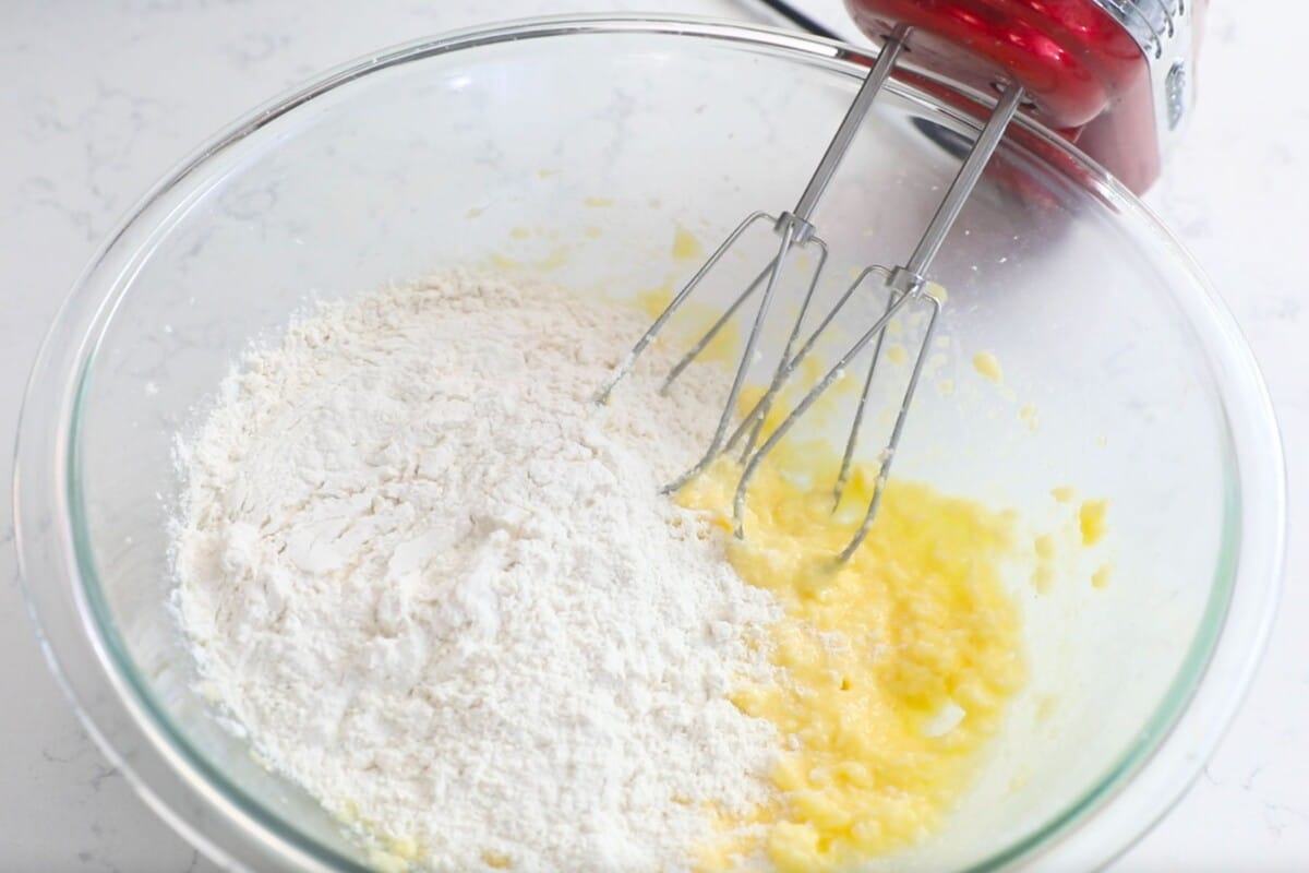 creamed cookie dough with flour in a large clear bowl with mixer.