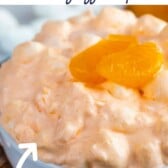 Orange jello salad in a small white bowl topped with mandarin oranges with recipe title on top of image