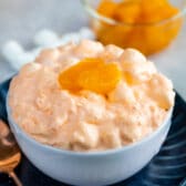 Orange jello salad in a small white bowl topped with mandarin oranges