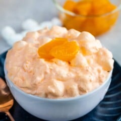 Orange jello salad in a small white bowl topped with mandarin oranges