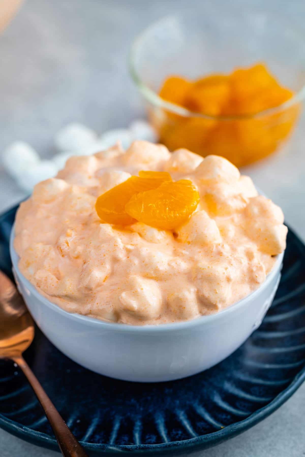 Orange jello salad in a small white bowl topped with mandarin oranges