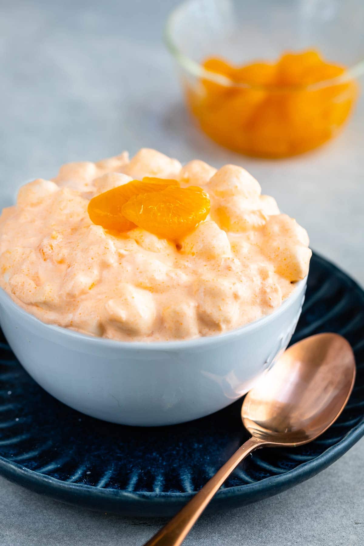 Orange jello salad in a small white bowl topped with mandarin oranges