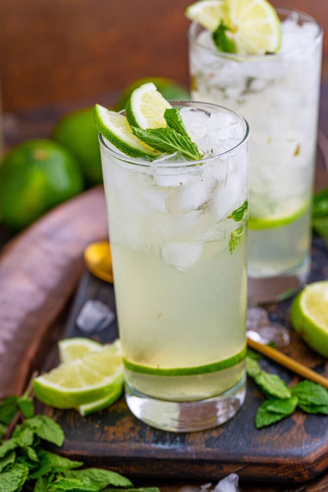 Two glasses of mojitos with lime and mint around them