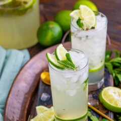 Two glasses of mojitos with lime and mint around them