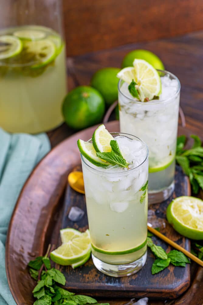 Two glasses of mojitos with lime and mint around them