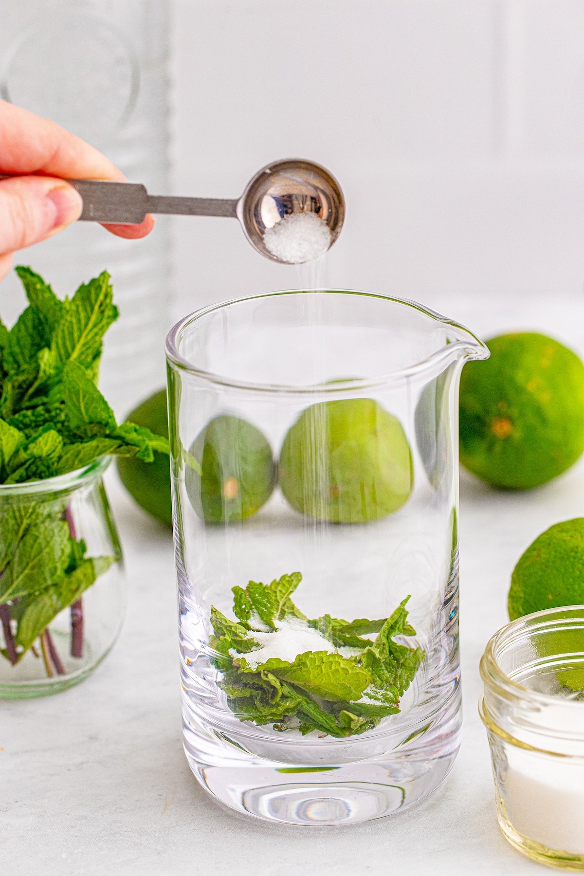 hand adding sugar to a glass with mint