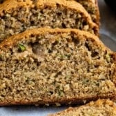 Close-up of sliced zucchini bread showing a moist, dense texture with visible bits of shredded zucchini. The golden brown crust is slightly crisp, while the soft interior offers a tempting look at this delicious zucchini bread recipe.