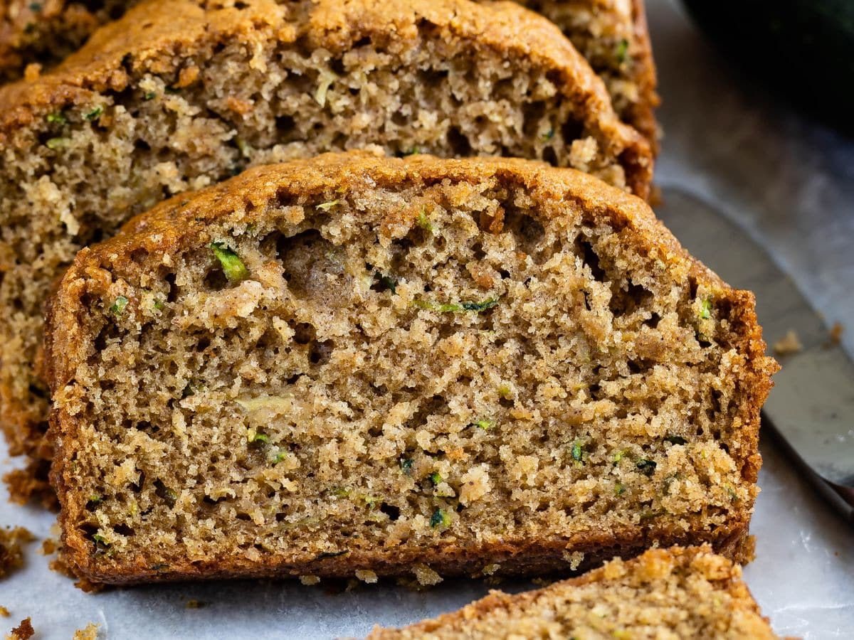 Close-up of sliced zucchini bread showing a moist, dense texture with visible bits of shredded zucchini. The golden brown crust is slightly crisp, while the soft interior offers a tempting look at this delicious zucchini bread recipe.