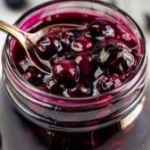 Blueberry pie filling in a small mason jar with spoon coming out of it with recipe title on top of image