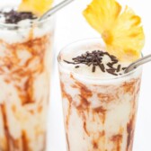 Two chocolate coladas with pineapple slices on top and recipe title on top of photo