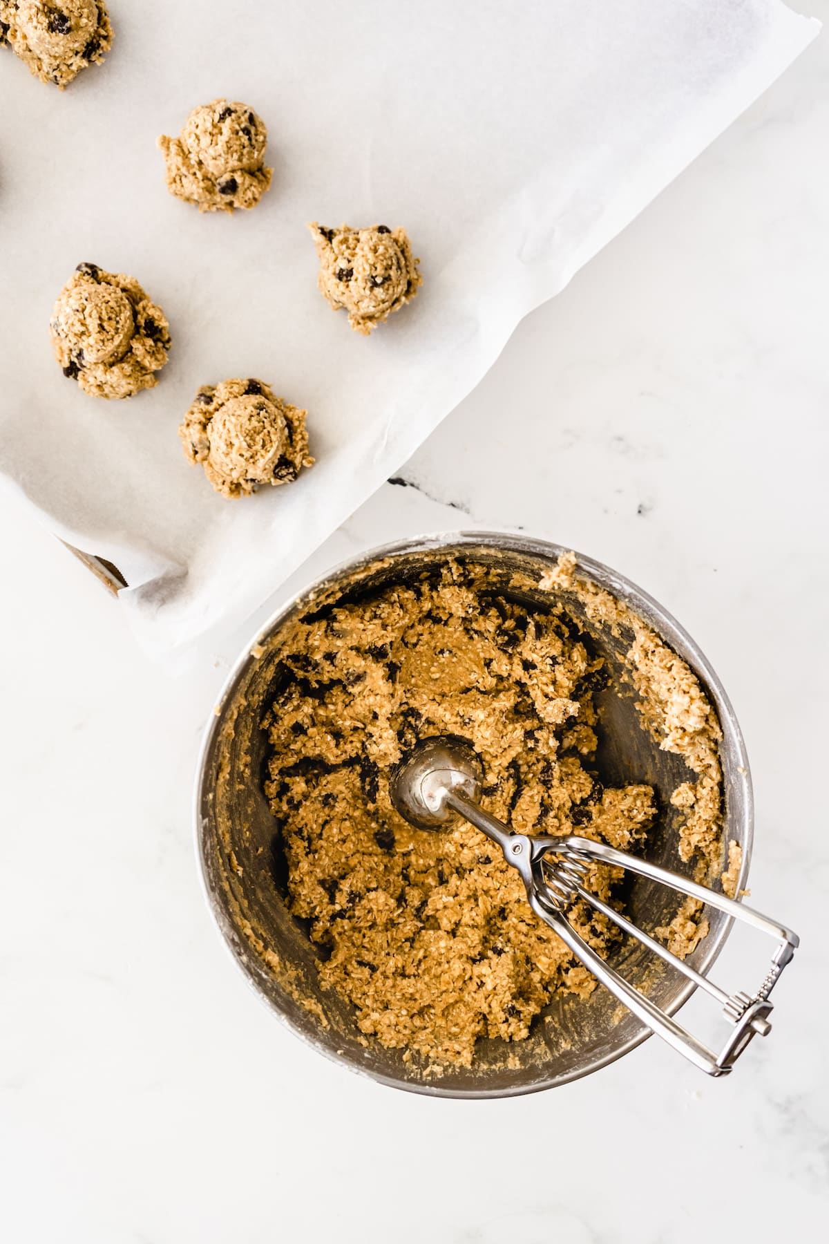 cookie dough in mixer bowl with scoop and cookie sheet with cookie dough balls on it