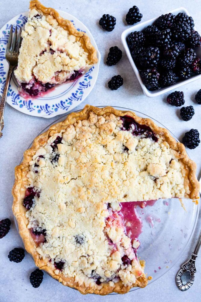 Overhead shot of blackberry pie with a crumble topping with one slice on a plate