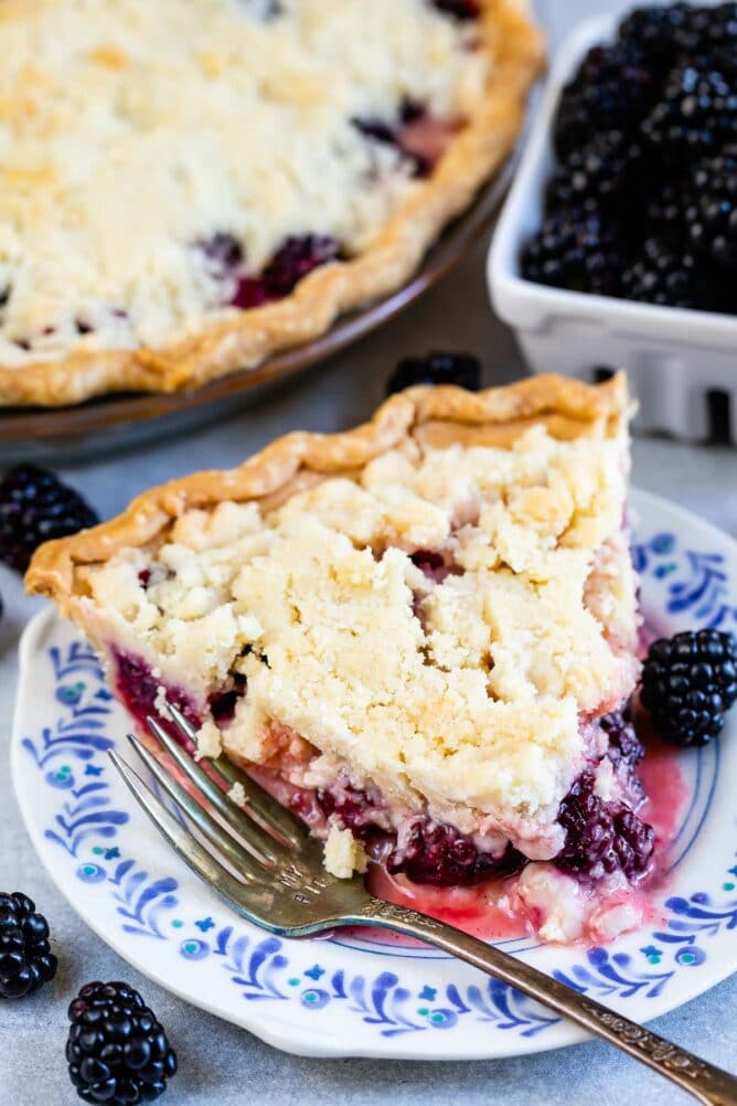 One slice of blackberry pie with crumble topping on a plate