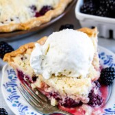 One slice of blackberry pie with crumble topping and a scoop of ice cream on top on a plate