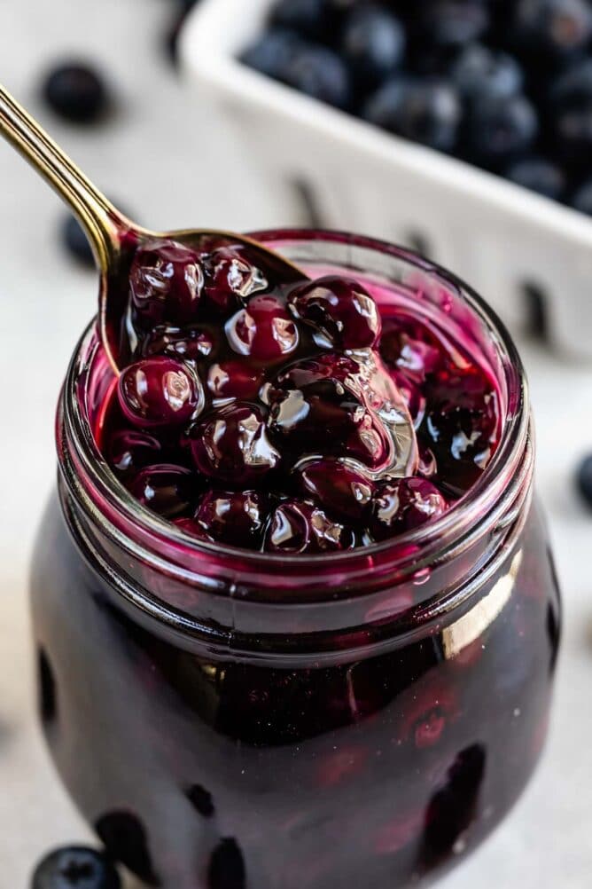 Blueberry pie filling in a small mason jar with spoon coming out of it