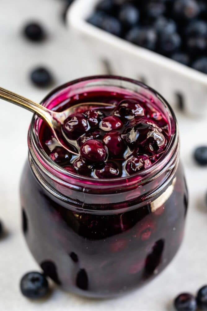 Blueberry pie filling in a small mason jar with spoon coming out of it