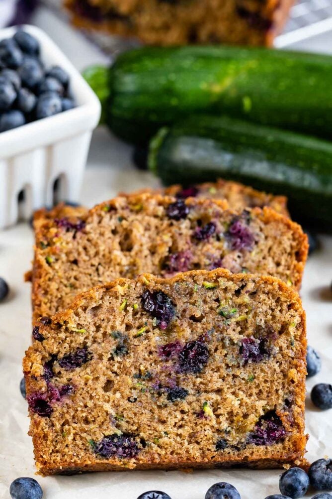 Three slices of blueberry zucchini bread with blueberries around it